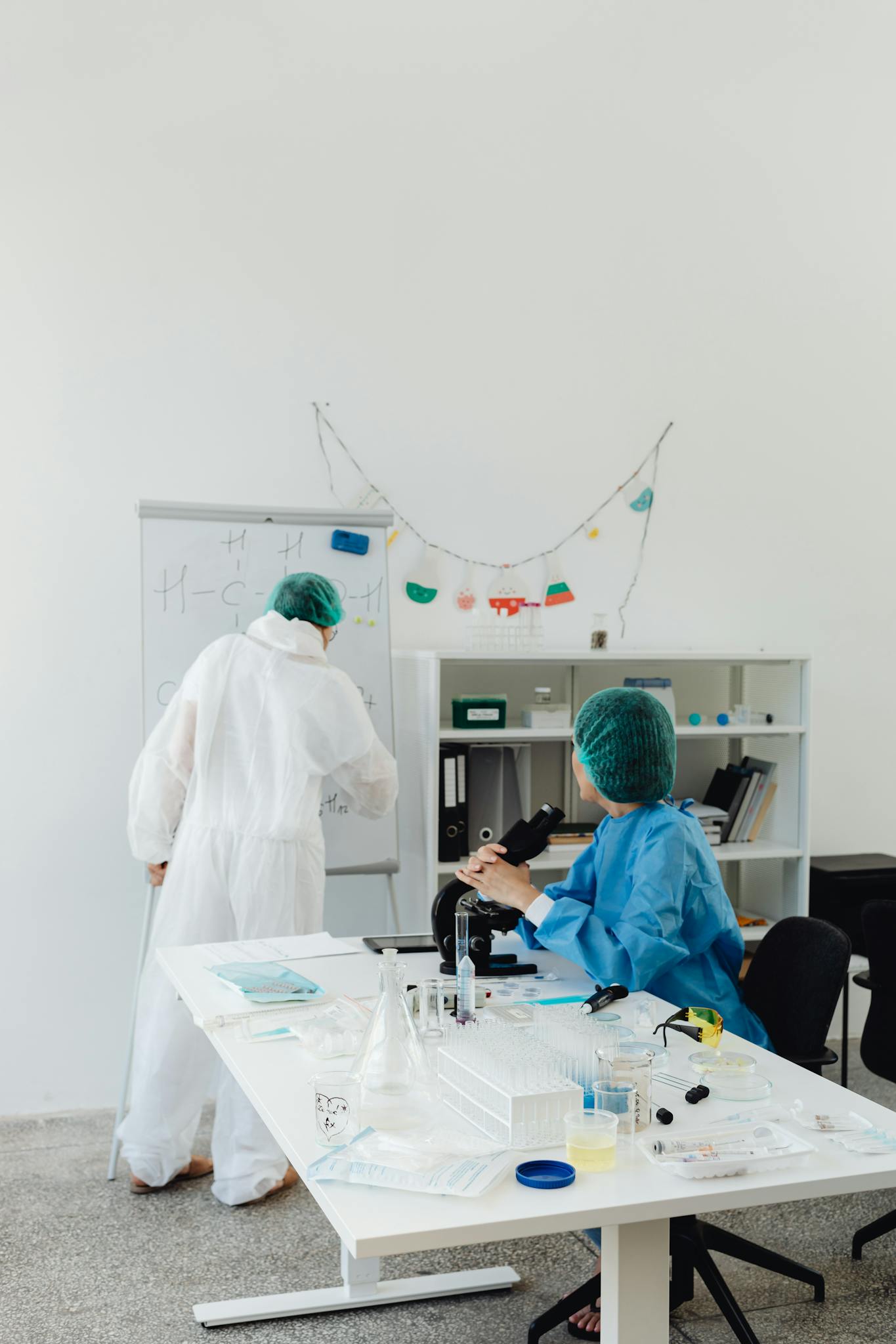 Scientists in lab coats conduct research with microscope and whiteboard in a bright laboratory setting.